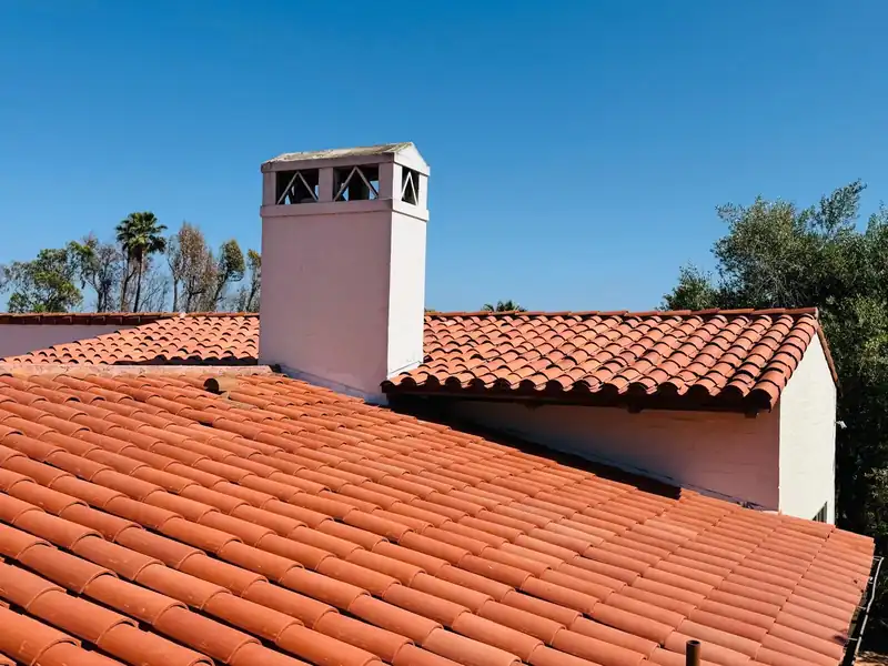 Clay barrel tile roof with a white stucco chimney on a Spanish style house under a clear sky