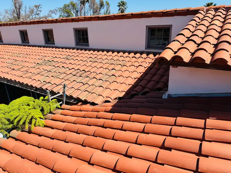 Close view of clay barrel tile courses on a stucco house, older weathered tile above and cleaner tile below