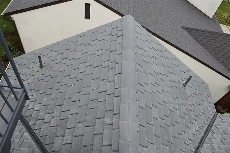 Slate-look composite tile roof meeting a white wall