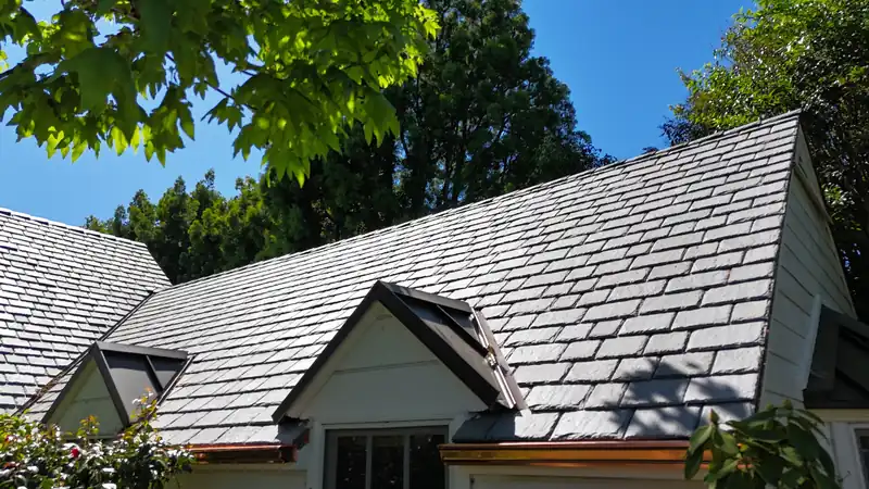 Slate-look composite roof with a gabled dormer and copper gutters among trees