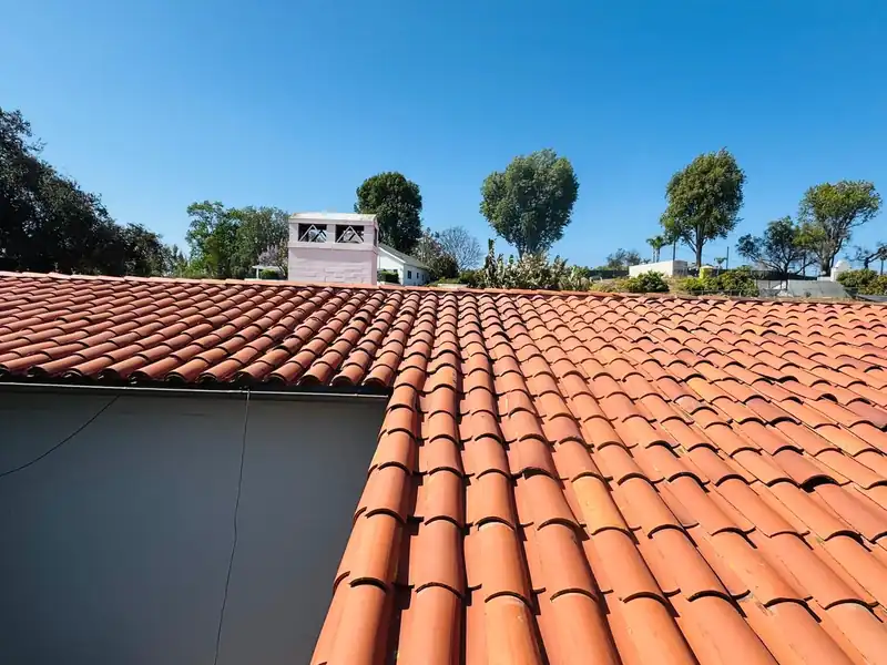 Freshly relaid red clay barrel tile roof field with a stucco chimney and treetops beyond
