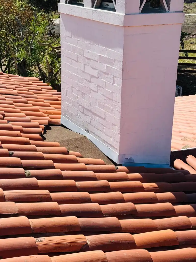 White stucco chimney with clay barrel tile laid neatly around its base