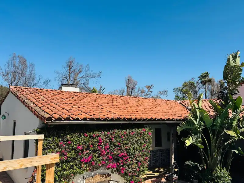 Red clay barrel tile roof over a white stucco house with bougainvillea along the wall