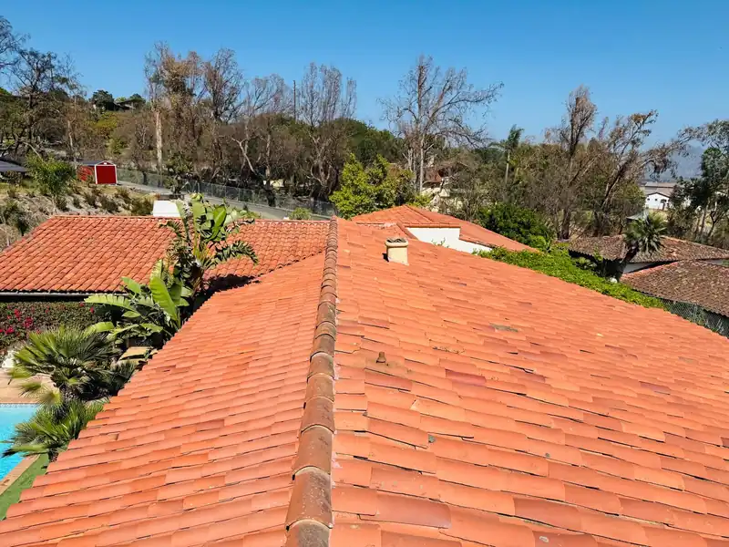 Clay barrel tile hip roof on a hillside house, with palms and a pool below