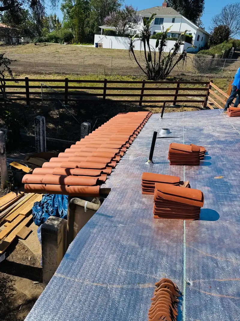 New clay barrel tiles staged in stacks on fresh reflective underlayment before they are laid