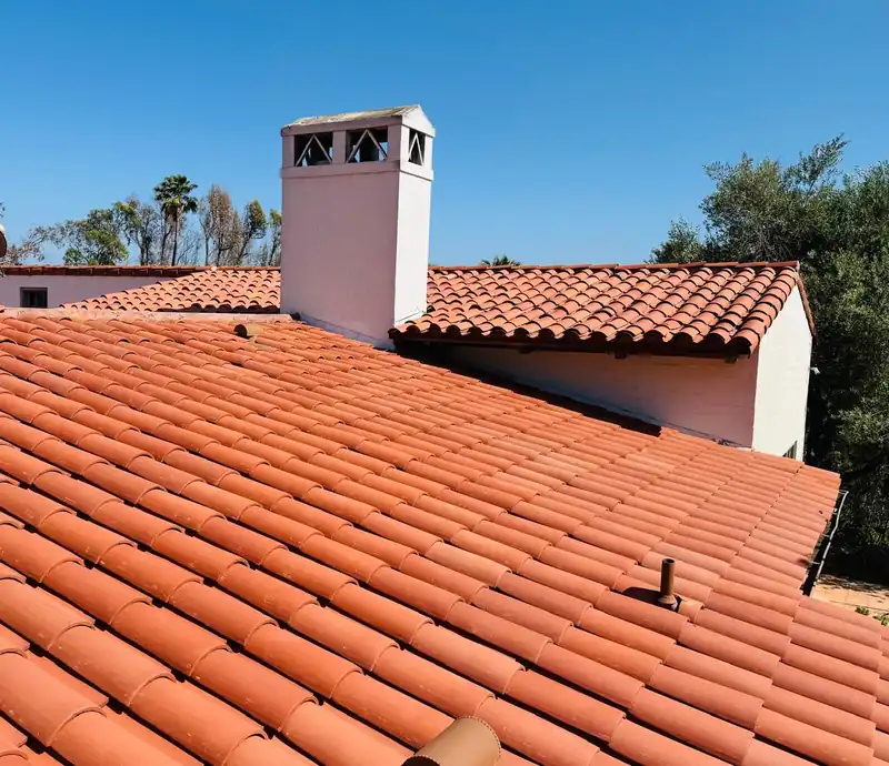 Finished clay barrel tile roof with a white stucco chimney and a matching tile ridge