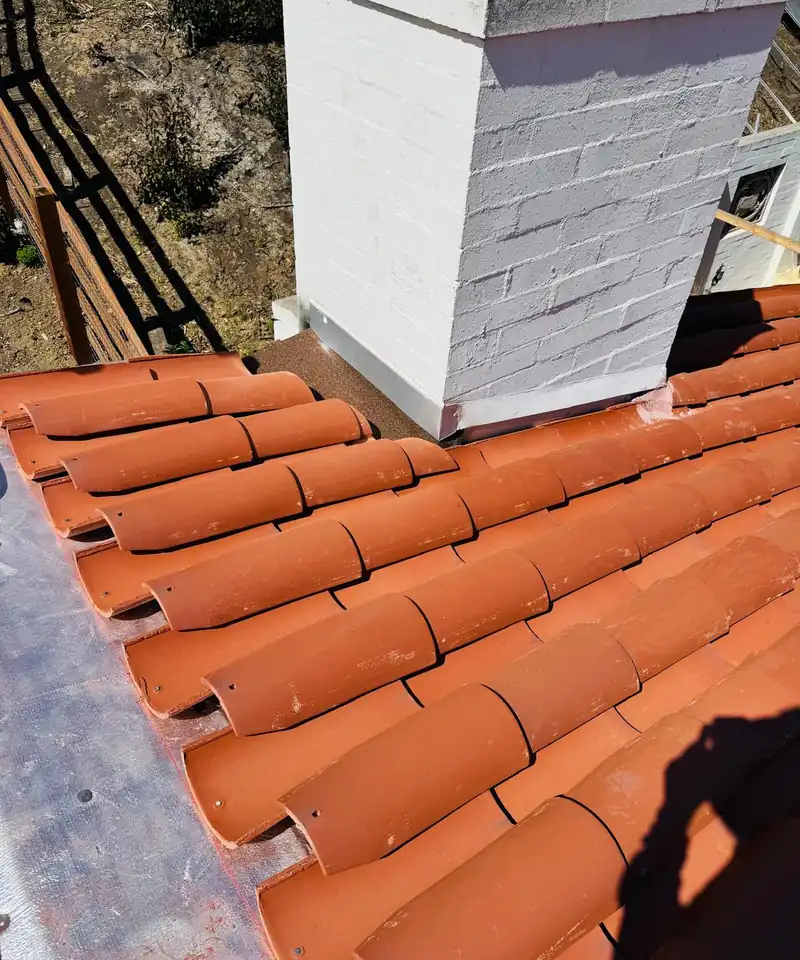 Clay barrel tile and new flashing laid neatly around the base of a stucco chimney